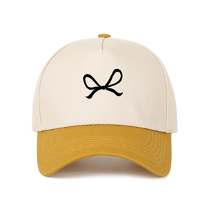 Close-up of the beige and yellow panel trucker hat featuring a black bow embroidery