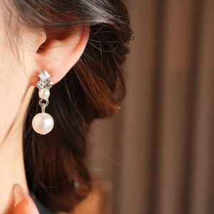 Close-up of elegant silver drop earrings with zircons and white pearls on model