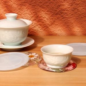Detail of floral resin coasters and white embossed porcelain tea set on wooden surface
