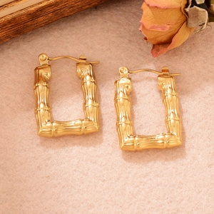 Vue macro de boucles d'oreilles en forme de U dorées texturées bambou sur velours beige