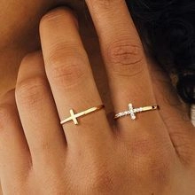 Primer plano de un anillo de cruz dorado con pequeñas circonitas y un anillo liso sencillo