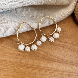 Close-up of golden hoop earrings with cream striped stone tassels on a wooden surface