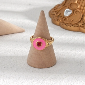 Détail macro d'une bague dorée avec émail rose et une pierre précieuse rouge en cœur