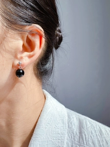Close-up of elegant silver drop earring featuring a polished black onyx bead on model