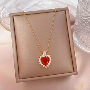 Detail of a gold titanium necklace featuring a faceted red heart pendant with small white stones