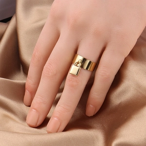 Close-up of wide gold stainless steel ring featuring a mini padlock charm on satin