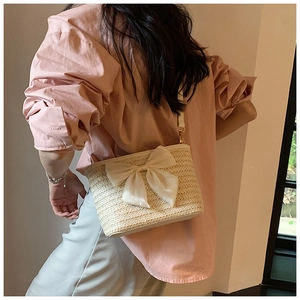 Detail of woven straw bucket bag with large satin bow accent and slender shoulder strap