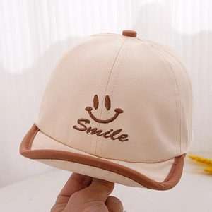 Détail de la casquette bébé en coton beige avec broderie Smile marron et visière courbée