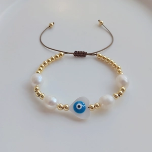 Handmade pearl and gold bead bracelet featuring a blue heart evil eye charm and brown cord