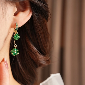 Close-up of vintage golden drop earrings with green crystals worn by a model