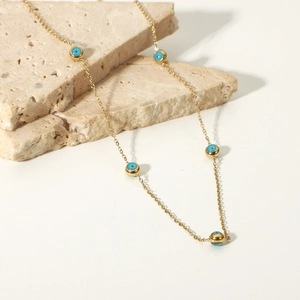 Macro detail of 18K gold plated chain with blue evil eye beads on stone background