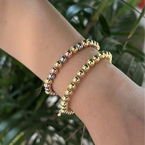 Detail of stacked gold and tri-color metallic bead bracelets on a model's wrist