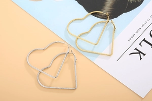 Detailed view of twisted heart hoop earrings in polished gold and silver finishes