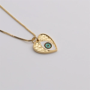 Détail macro du pendentif cœur doré avec motif œil grec et finition martelée mate