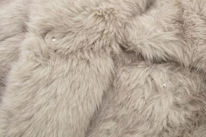 Close-up of fluffy faux fur texture in beige with a detailed silver metal button
