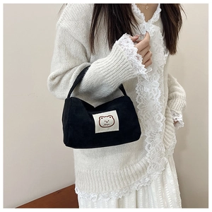 Detail of black corduroy handbag with cute bear patch worn with a white sweater