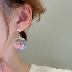 Iridescent shell-shaped dangle earrings with white pearl detail on model ear