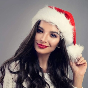 Classic plush red Santa hat with large white faux fur pompom worn by a female model