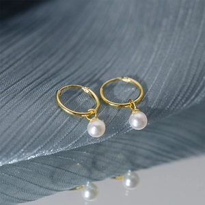 Detailed close-up of golden pearl hoop earrings resting on blue silk with mirror reflection