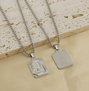 Macro shot of silver stainless steel rectangular pendant with J letter and grid texture