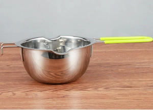 Close-up of a stainless steel melting pot with lime green handle on a wooden table