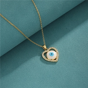 Gold heart necklace with evil eye pendant and crystal border on blue fabric