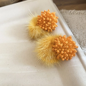 Detailed shot of yellow beaded flower and faux fur pom-pom earrings on a white tray