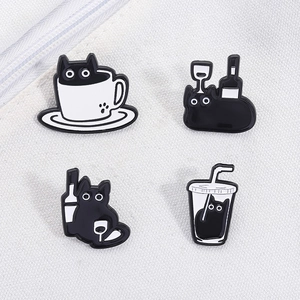 Detailed set of four black enamel cat pins in coffee cups and wine bottles on white fabric