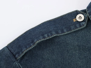 Détail de l'épaulette avec bouton métallique et coutures contrastées sur veste en jean