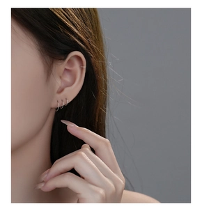 Close-up of a model wearing three minimalist S999 silver hoop earrings and one ear cuff