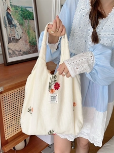 Off-white canvas tote bag with floral embroidery held by model in vintage room