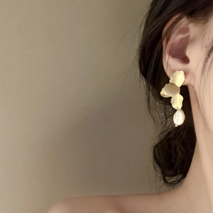 Detailed view of golden petal stud earrings with baroque pearl drop on a model