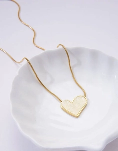 Detailed close-up of a golden heart pendant necklace resting in a white shell-shaped dish