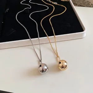 Minimalist ball pendant necklaces in polished gold and silver on jewelry display tray