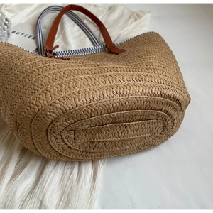 Minimalist straw woven tote bag with brown handles and striped lining for beach holidays