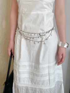 Detail of silver layered waist chain with pearls and shell pendant on a white dress