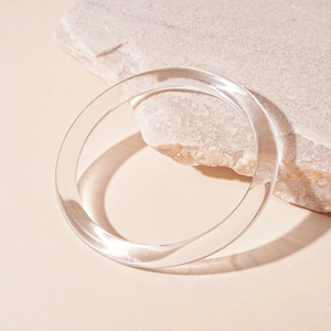 Close-up of minimalist transparent acrylic round bangle on natural pink marble texture