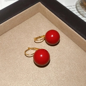 Close-up of luxury gold-plated leverback earrings with glossy red resin sphere drops