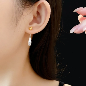 Close-up of gold stud and silver teardrop earrings worn by a model on black background