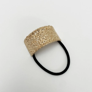 Detail of a matte gold U-shaped hair tie with hammered texture and black elastic band