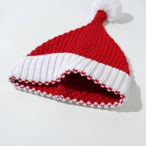Detail view of red knitted Christmas hat featuring white pom-pom and thick ribbed texture