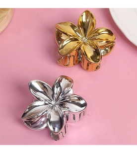Macro detail of gold and silver metal flower hair claw clips on a pink background