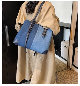 Detail view of large denim tote bag with contrast stitching on a model in trench coat