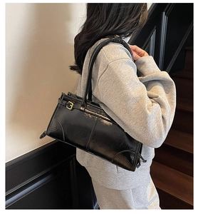 Detailed view of a sleek black underarm bag with gold hardware worn by a model