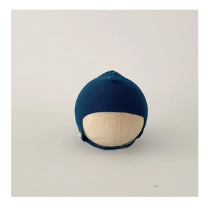 Detail of navy knit baby beanie with side button and chin strap on wooden stand