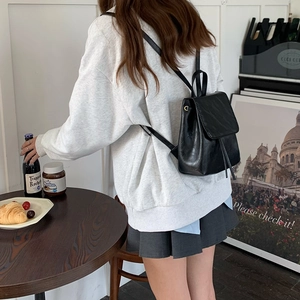 Vista laterale di un piccolo zaino in pelle nera indossato da una modella al caffè