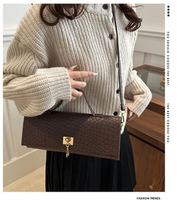 Detail of dark brown crocodile textured handbag with luxury gold buckle and strap