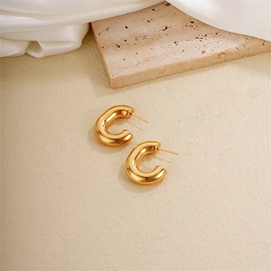 Close-up of polished gold-plated titanium steel C-shaped hoop earrings on natural stone