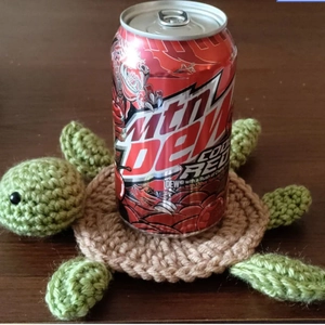 Macro shot of green and brown hand-crocheted turtle coaster on dark wooden surface