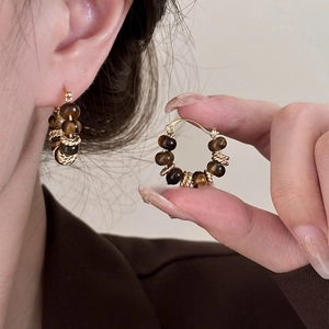 Detail of tiger eye stone earrings with twisted gold metal rings on a model's ear